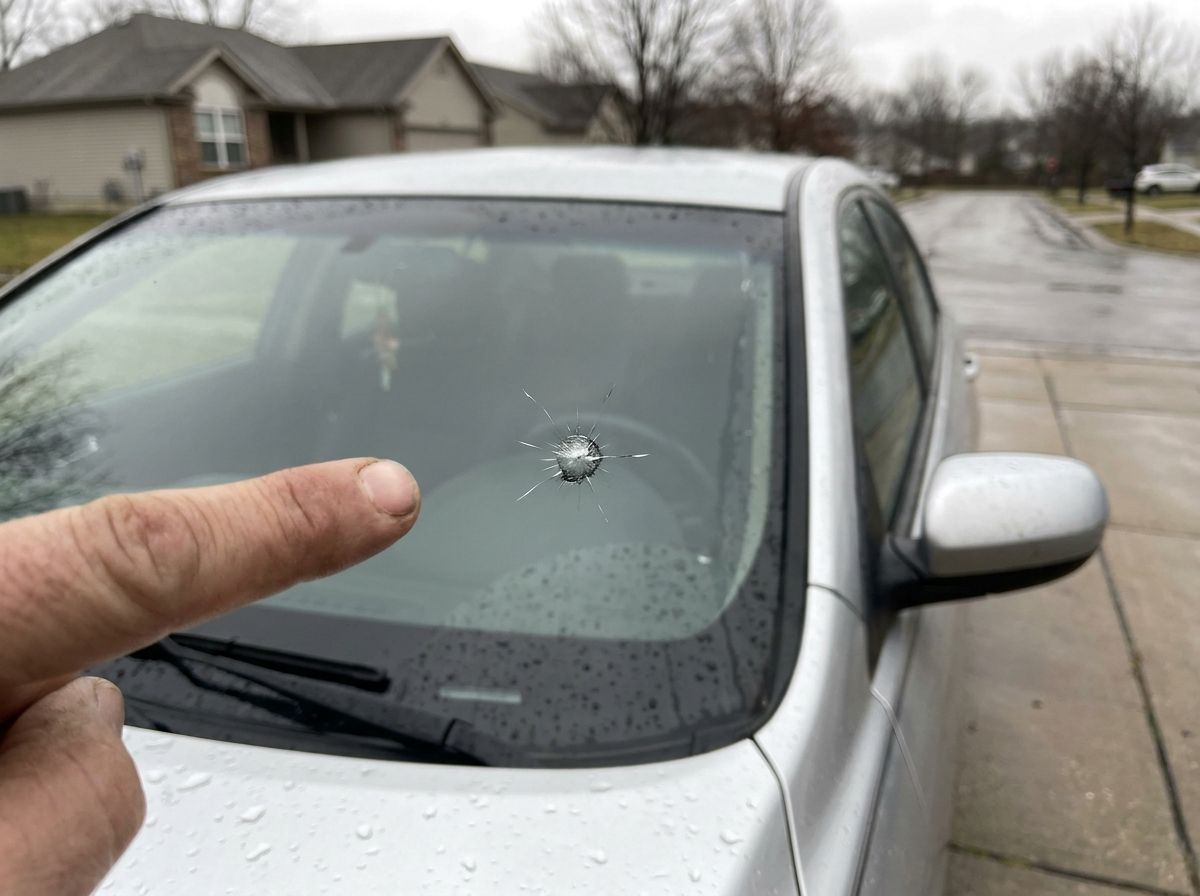 Finger pointing at a star-shaped rock chip on a car windshield in a Missouri driveway